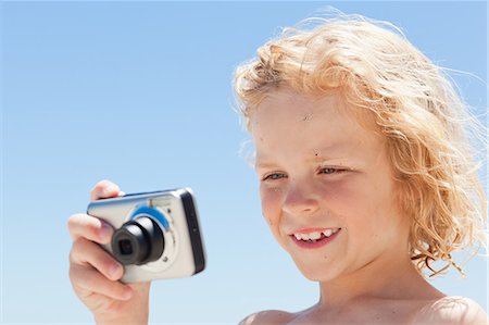 Smiling little boy looking at the screen of digital camera at the beach Stock Photo - Premium Royalty-Free, Code: 6109-06003775