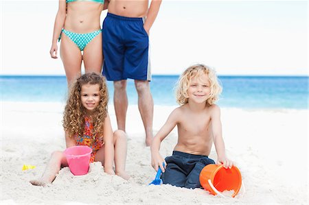 Little children building sandcastles with their parents behind them Stock Photo - Premium Royalty-Free, Code: 6109-06003851