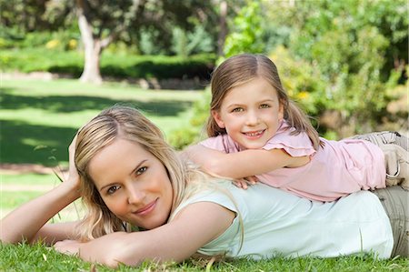 A smiling mother and daughter as the girl rests on top of her mothers back in the park Stock Photo - Premium Royalty-Free, Code: 6109-06003990