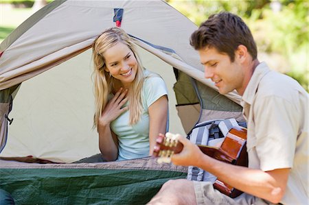 simsearch:6109-06003893,k - A man playing the guitar to impress his girlfriend as they camp together Stock Photo - Premium Royalty-Free, Code: 6109-06003903