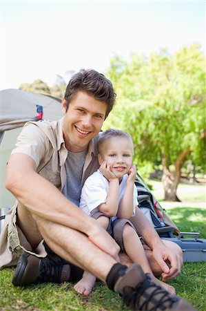 A smiling dad and son sit together just outside of the tent Stock Photo - Premium Royalty-Free, Code: 6109-06003917