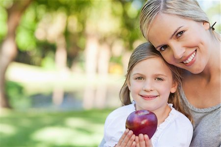 family gardening - A mother holding her daughter in her arms as the daughter holds a red apple Stock Photo - Premium Royalty-Free, Code: 6109-06004055