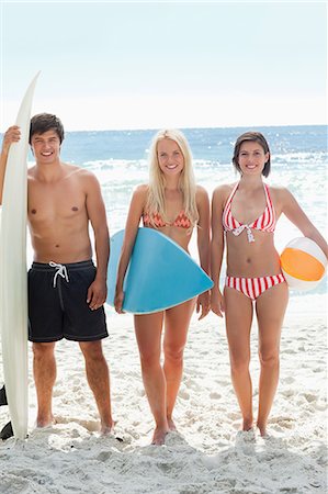 simsearch:6109-06004195,k - Man and two women standing on the beach in swimsuits as they are holding surfboards and a beach ball Stock Photo - Premium Royalty-Free, Code: 6109-06004201