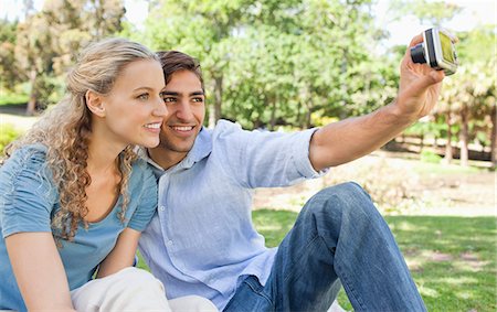 Side view of a smiling young couple taking a picture of themselves in the park Stock Photo - Premium Royalty-Free, Code: 6109-06004382