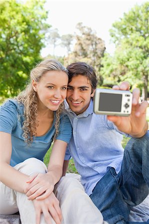 Smiling young couple taking pictures of themselves in the park Stock Photo - Premium Royalty-Free, Code: 6109-06004387