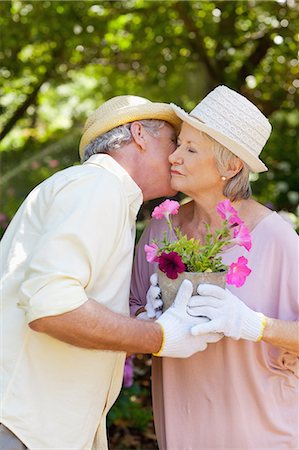 Woman getting a kiss on the cheek from a man while exchanging a pot of pink flowers Stock Photo - Premium Royalty-Free, Code: 6109-06004592