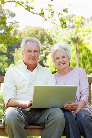 people sitting on bench - Man and a woman smiling as they sit together on a bench while holding a laptop Stock Photo - Premium Royalty-Free, Code: 6109-06004628