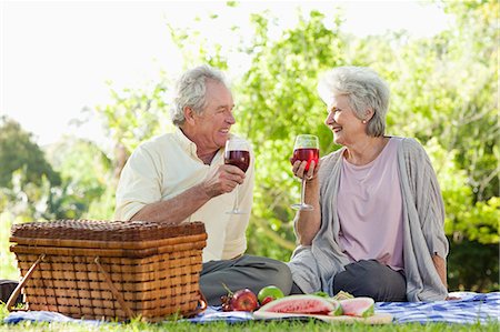 Couple holding glasses of red wine while looking at each other during a picnic in a park Stock Photo - Premium Royalty-Free, Code: 6109-06004773