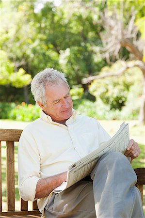 Man looking at a newspaper while sitting on a wooden bench in a park Stock Photo - Premium Royalty-Free, Code: 6109-06004718