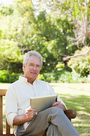 people sitting on bench - Man looking to his right side while holding a tablet as he sits in a park Stock Photo - Premium Royalty-Free, Code: 6109-06004733