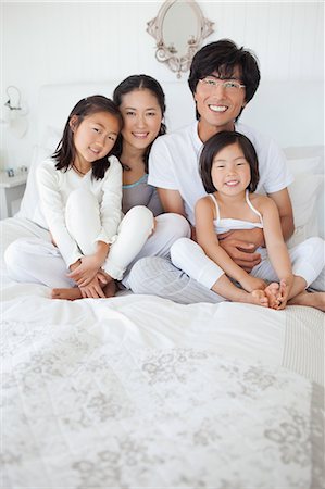 family portrait asian not grandparent - A family embraces each other as they all sit on the bed smiling Stock Photo - Premium Royalty-Free, Code: 6109-06005009