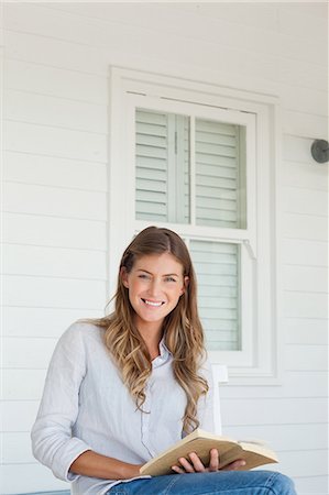 photo of person sitting on porch - A woman with a book in her hands smiles as she sits outside on the porch Stock Photo - Premium Royalty-Free, Code: 6109-06005198