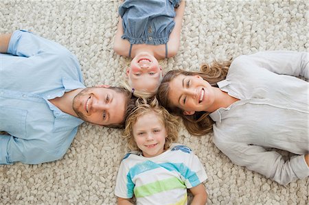 A family lying on the ground with their heads all together as they look up and smile at the camera Stock Photo - Premium Royalty-Free, Code: 6109-06005116