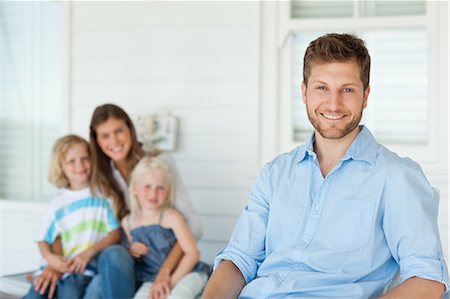 photo of person sitting on porch - A smiling father sits in front by himself while his wife and kids sit together in the back Stock Photo - Premium Royalty-Free, Code: 6109-06005217