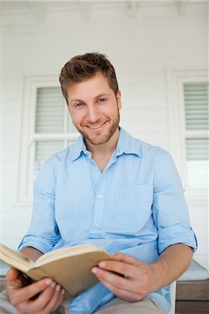 Un homme souriant avec un livre ouvert dans ses mains est assis sur le porche Photographie de stock - Premium Libres de Droits, Code: 6109-06005223