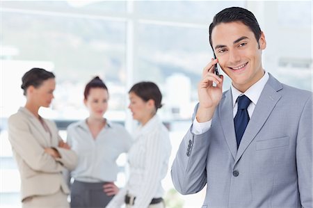 società - Smiling young businessman on his cellphone with colleagues behind him Fotografie stock - Premium Royalty-Free, Codice: 6109-06005659