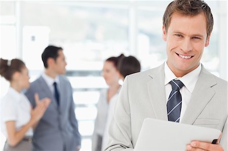 Smiling young salesman with his tablet computer and colleagues behind him Stock Photo - Premium Royalty-Free, Code: 6109-06005683