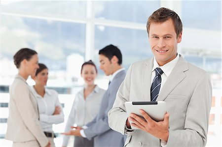 Smiling young salesman with tablet computer and colleagues behind him Stock Photo - Premium Royalty-Free, Code: 6109-06005682