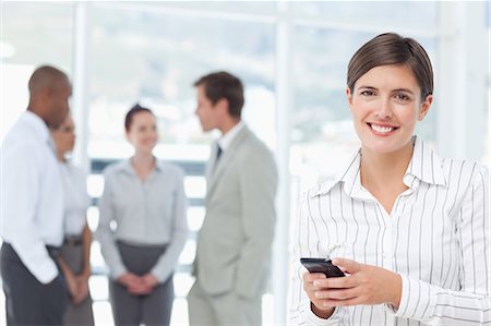 Smiling young saleswoman with cellphone and associates behind her Stock Photo - Premium Royalty-Free, Code: 6109-06005707