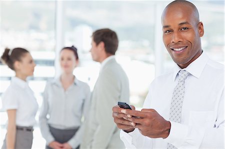 Smiling young salesman with his cellphone and associates behind him Stock Photo - Premium Royalty-Free, Code: 6109-06005735