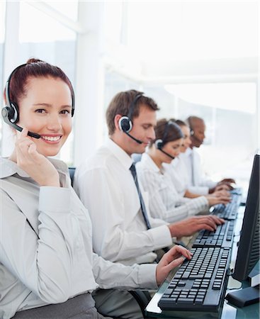 Smiling young call center employees sitting with her colleagues behind her Stock Photo - Premium Royalty-Free, Code: 6109-06005812