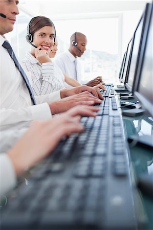 Smiling young call center agent adjusting her headset while sitting among colleagues Stock Photo - Premium Royalty-Free, Code: 6109-06005822