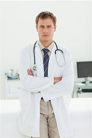 Serious male doctor with arms folded standing in his examination room Stock Photo - Premium Royalty-Free, Code: 6109-06006358