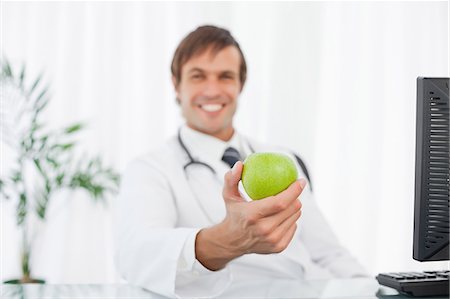 Beautiful green apple being held by a happy surgeon sitting at his desk Stock Photo - Premium Royalty-Free, Code: 6109-06006865