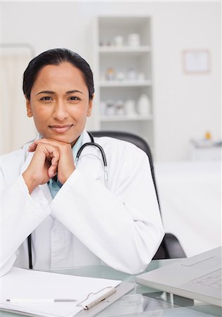 Serious doctor sitting with her elbows on the desk while looking at the camera Stock Photo - Premium Royalty-Free, Code: 6109-06006899