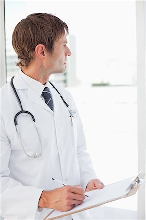simsearch:6109-06006928,k - Surgeon holding his clipboard while standing upright and looking outside Stock Photo - Premium Royalty-Free, Code: 6109-06006800