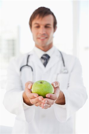 Delicious green apple is in the hands of a smiling surgeon standing in front of a window Stock Photo - Premium Royalty-Free, Code: 6109-06006807