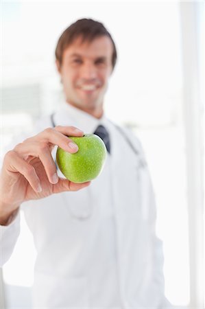 A smiling surgeon is holding a delicious green apple in front of a window Stock Photo - Premium Royalty-Free, Code: 6109-06006804