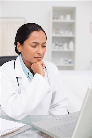 simsearch:6109-06006928,k - Serious doctor placing her chin on her fist while looking at her laptop Stock Photo - Premium Royalty-Free, Code: 6109-06006917