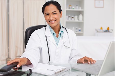 simsearch:6109-06006928,k - Smiling doctor sitting at her desk while hanging up the phone Stock Photo - Premium Royalty-Free, Code: 6109-06006914
