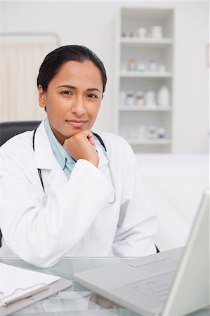 simsearch:6109-06006928,k - Serious doctor looking at the camera while sitting behind her laptop Stock Photo - Premium Royalty-Free, Code: 6109-06006918