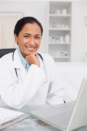 simsearch:6109-06006928,k - Smiling doctor sitting in front of her laptop with her hand on her chin Stock Photo - Premium Royalty-Free, Code: 6109-06006919