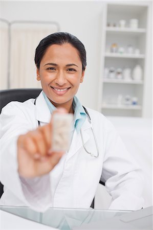 simsearch:6109-06006928,k - Smiling doctor holding pills while sitting at her desk Stock Photo - Premium Royalty-Free, Code: 6109-06006921