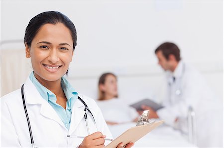 Surgeon holding a clipboard while smiling and standing in a hospital bedroom Stock Photo - Premium Royalty-Free, Code: 6109-06007051