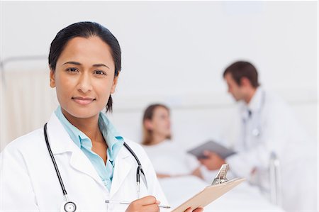 simsearch:6109-06006928,k - Relaxed surgeon writing on her clipboard while standing up in a private hospital room Stock Photo - Premium Royalty-Free, Code: 6109-06007052