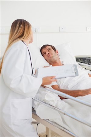 Patient lying in a hospital bed while looking at his nurse who is holding a clipboard Stock Photo - Premium Royalty-Free, Code: 6109-06007090