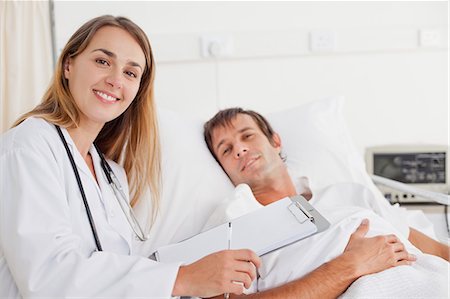 doctor nurse and patient men - Smiling nurse staring at the camera while standing next to a patient lying in a bed Stock Photo - Premium Royalty-Free, Code: 6109-06007092
