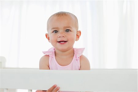 Happy baby standing in her bed while smiling and staring at the camera Stock Photo - Premium Royalty-Free, Code: 6109-06007024