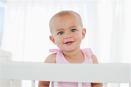 Lovely baby smiling and staring at the camera while standing up in her bed Foto de stock - Sin royalties Premium, Código: 6109-06007025