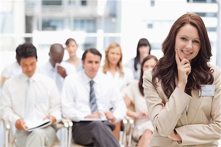 Smiling businesswoman holding her hand to her face as she stands in front of her co-workers Stock Photo - Premium Royalty-Free, Code: 6109-06007261