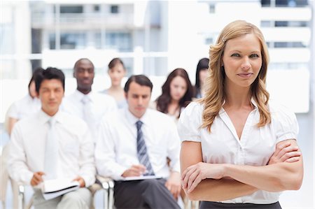 Brunette haired businesswoman looking ahead of her with a serious expression and her arms crossed as she stands in front of her colleagues Stock Photo - Premium Royalty-Free, Code: 6109-06007264