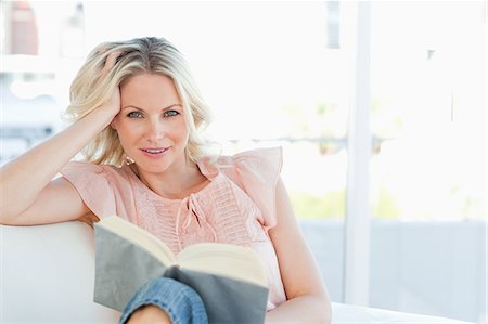 Smiling female lying on a sofa while reading a book Stock Photo - Premium Royalty-Free, Code: 6109-06194278