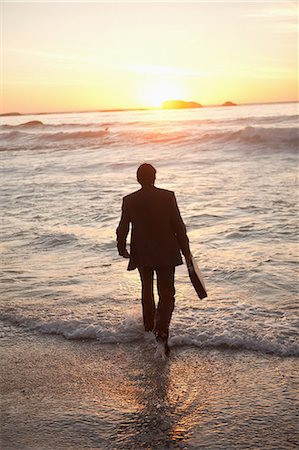 Young businessman walking in the water with his briefcase Stock Photo - Premium Royalty-Free, Code: 6109-06195407