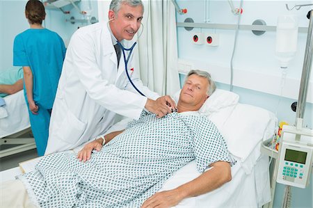 simsearch:6109-06196363,k - Smiling male doctor auscultating the chest of a male patient in a bed ward Stock Photo - Premium Royalty-Free, Code: 6109-06196261