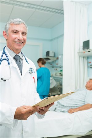 simsearch:6109-06196363,k - Smiling doctor looking at a chart in a bed ward Stock Photo - Premium Royalty-Free, Code: 6109-06196268