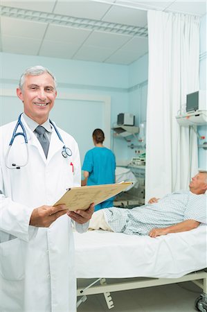simsearch:6109-06196363,k - Happy doctor holding a chart in a bed ward Stock Photo - Premium Royalty-Free, Code: 6109-06196270